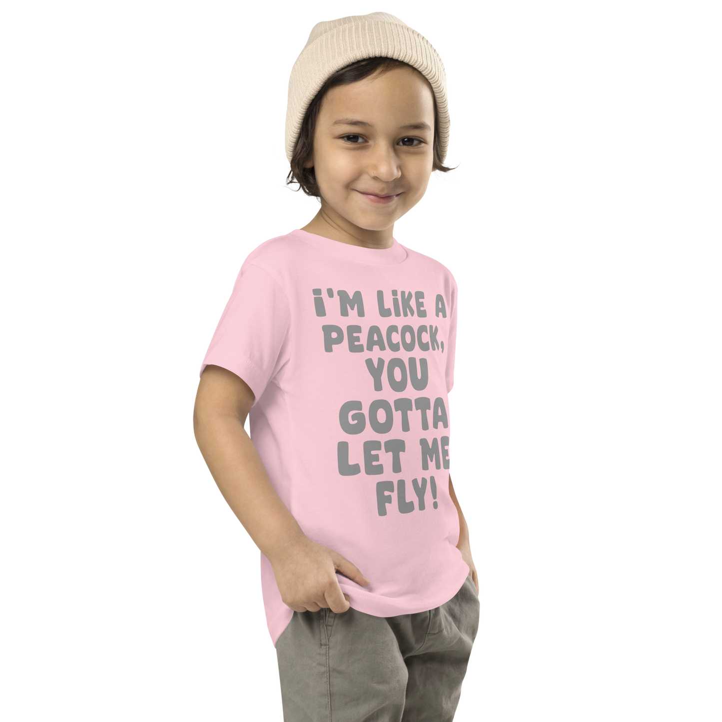 "I'm like a peacock, you gotta let me fly!" printed on a pink toddler short sleeve tee worn by a male who is also wearing a knit cap
