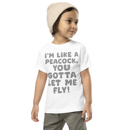 "I'm like a peacock, you gotta let me fly!" printed on a white toddler short sleeve tee worn by a male wearing a cap