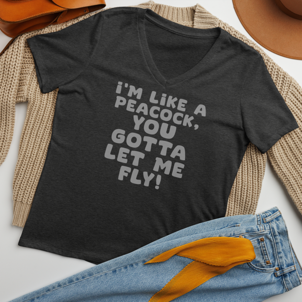 "I'm like a peacock, you gotta let me fly!" printed on a dark grey heather women's relaxed v-neck t-shirt laying on a flat surface amongst other clothes