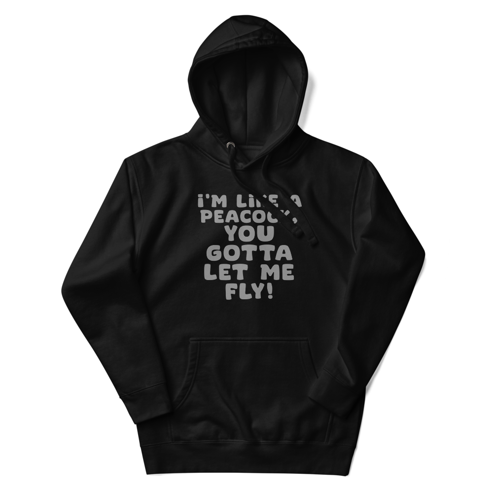 "I'm like a peacock, you gotta let me fly!" printed on a black unisex hoodie laying on a flat surface with the hood up