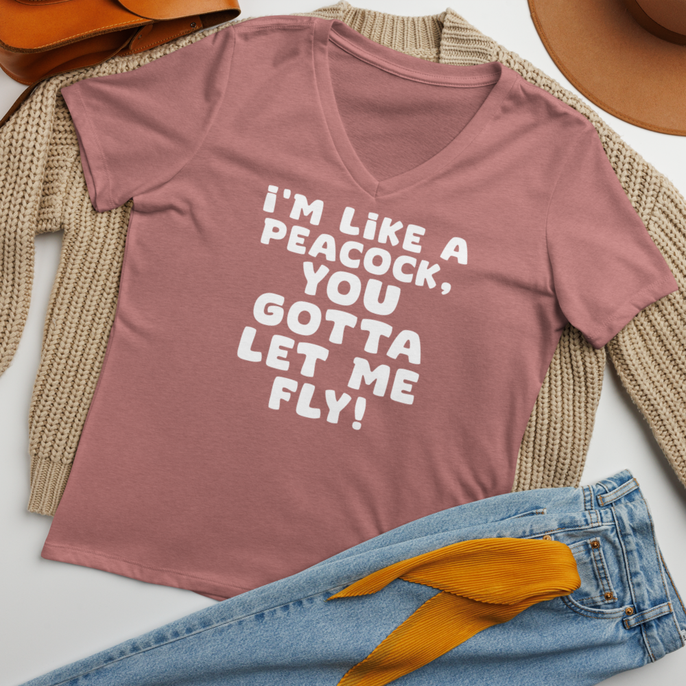 "I'm like a peacock, you gotta let me fly!" printed on a heather mauve women's relaxed v-neck t-shirt laying on a flat surface amongst other clothes