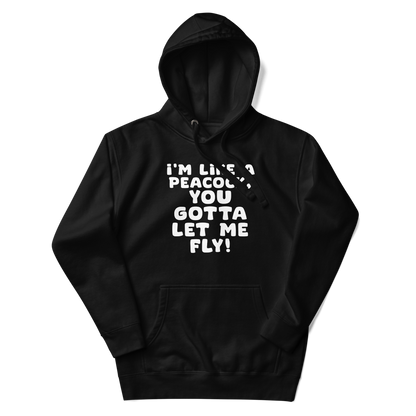 "I'm like a peacock, you gotta let me fly!" printed on a black unisex hoodie laying on a flat surface with the hood up