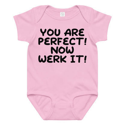 "You Are Perfect! Now Werk It!" printed on a pink baby jersey bodysuit laying on a flat surface amongst other clothes