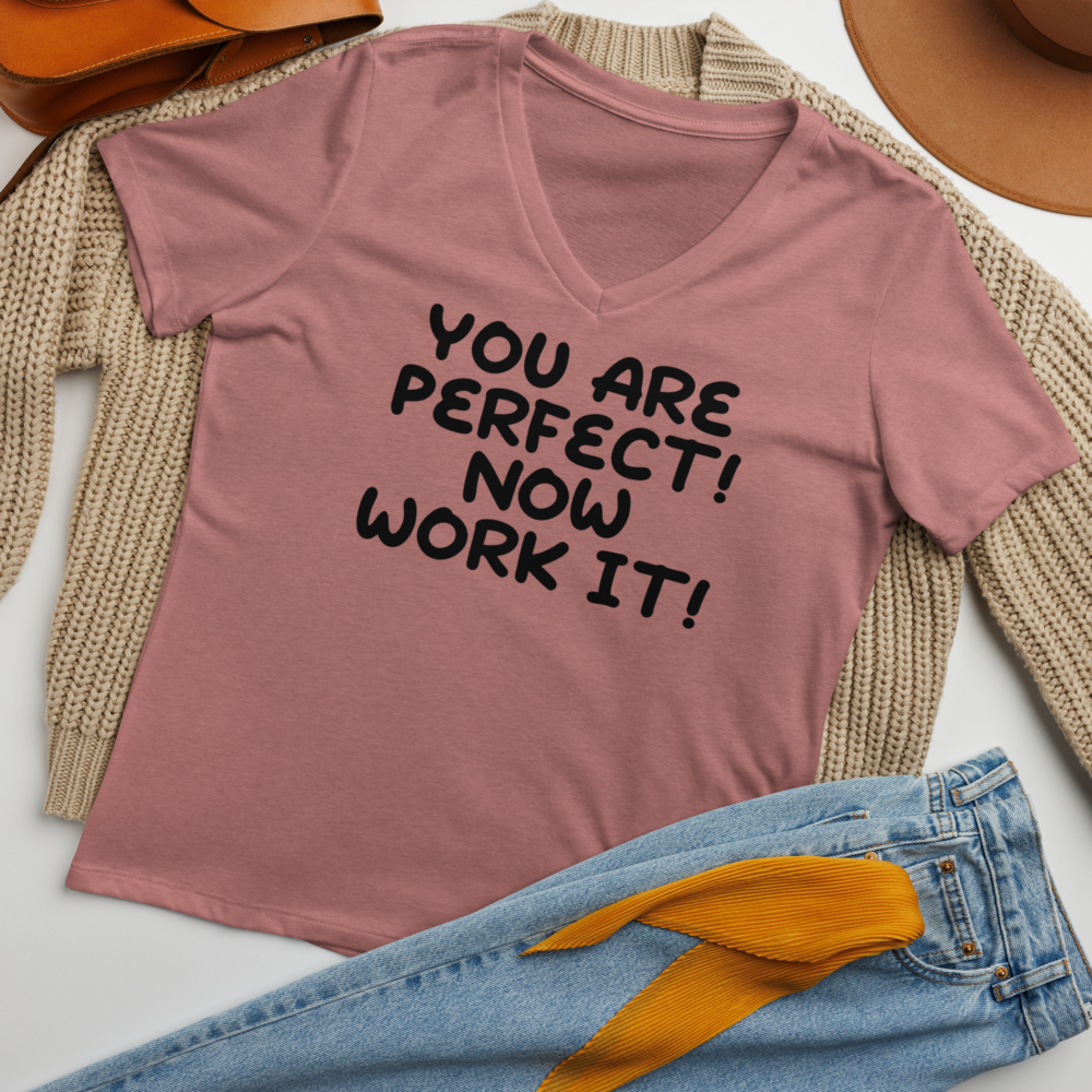 "You Are Perfect! Now Work It!" printed on a heather mauve women's relaxed v-neck t-shirt laying on a flat surface amongst other clothes