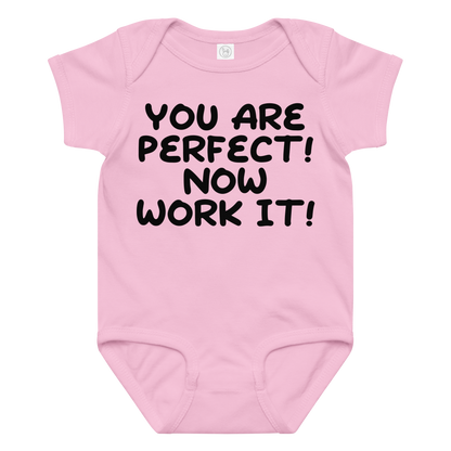 "You Are Perfect! Now Work It!" printed on a pink baby jersey bodysuit laying on a flat surface amongst other clothes