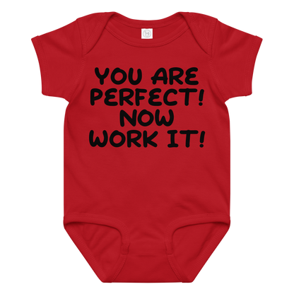 "You Are Perfect! Now Work It!" printed on a red baby jersey bodysuit laying on a flat surface amongst other clothes