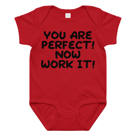 "You Are Perfect! Now Work It!" printed on a red baby jersey bodysuit laying on a flat surface amongst other clothes