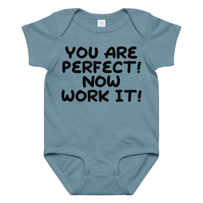 "You Are Perfect! Now Work It!" printed on a vintage indigo baby jersey bodysuit laying on a flat surface amongst other clothes