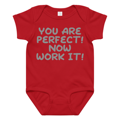 "You Are Perfect! Now Work It!" printed on a red baby jersey bodysuit laying on a flat surface amongst other clothes