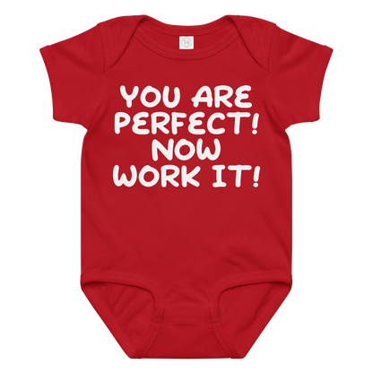 "You Are Perfect! Now Work It!" printed on a red baby jersey bodysuit laying on a flat surface amongst other clothes