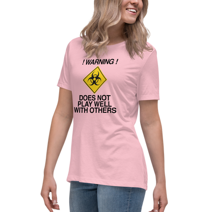 "!Warning! Does Not Play Well With Others" printed on a pink women's relaxed t-shirt worn by a female