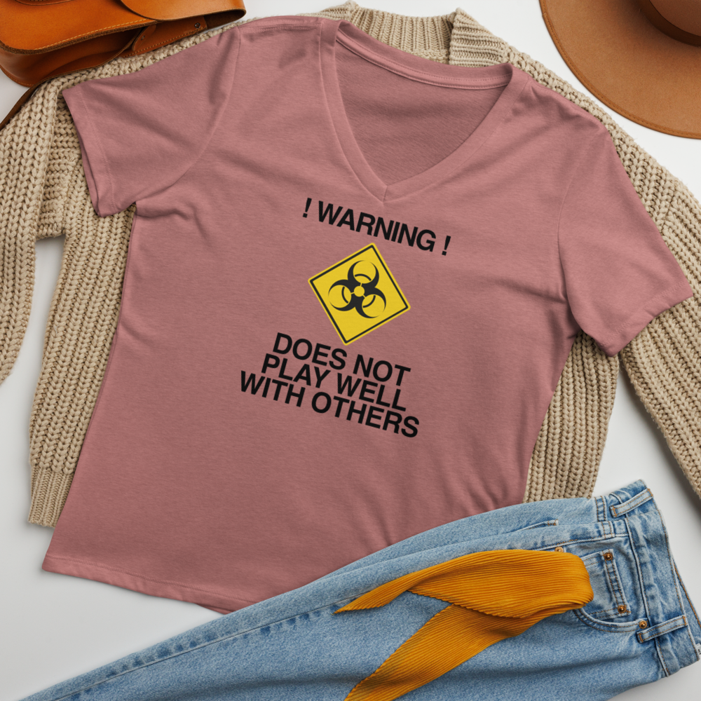 "!Warning! Does Not Play Well With Others" printed on a heather mauve women's relaxed v-neck t-shirt laying on a flat surface amongst other clothes