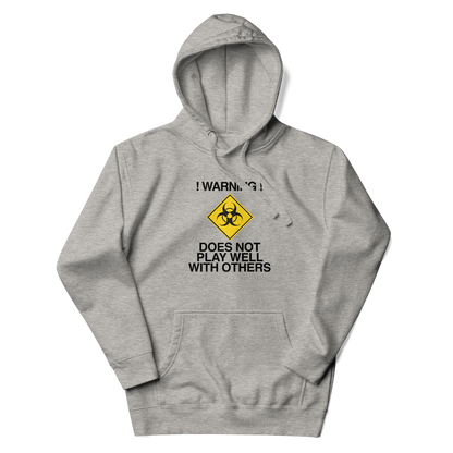"!Warning! Does Not Play Well With Others" printed on a carbon grey unisex hoodie laying on a flat surface with the hood up