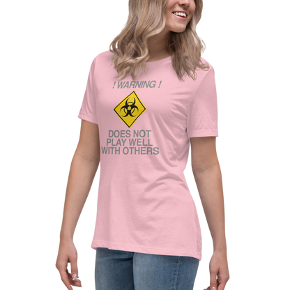 "!Warning! Does Not Play Well With Others" printed on a pink women's relaxed t-shirt worn by a female