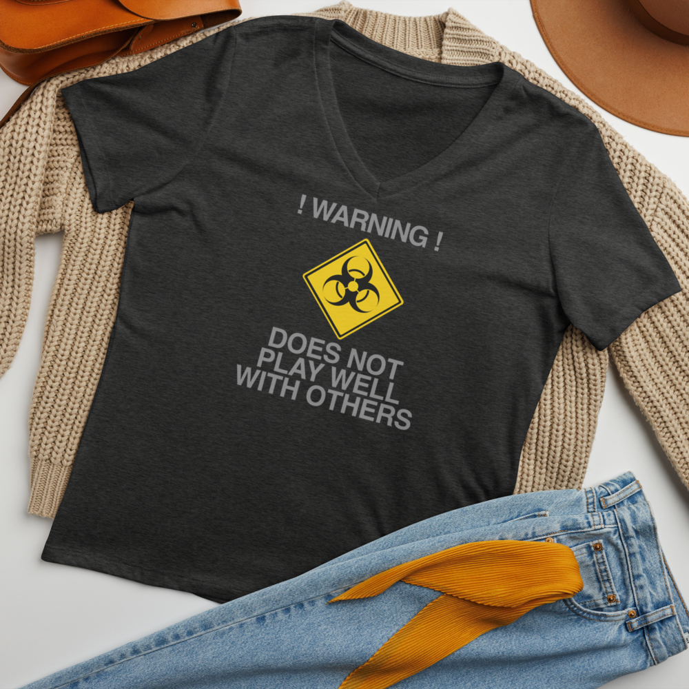 "!Warning! Does Not Play Well With Others" printed on a dark grey heather women's relaxed v-neck t-shirt laying on a flat surface amongst other clothes