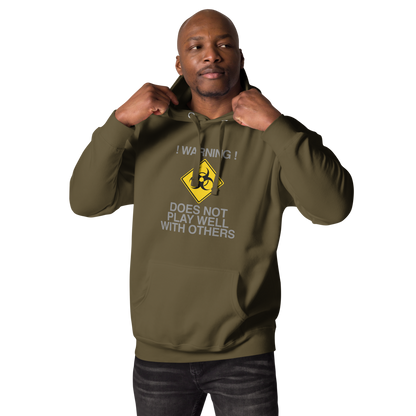 "!Warning! Does Not Play Well With Others" printed on a military green unisex hoodie worn by a male