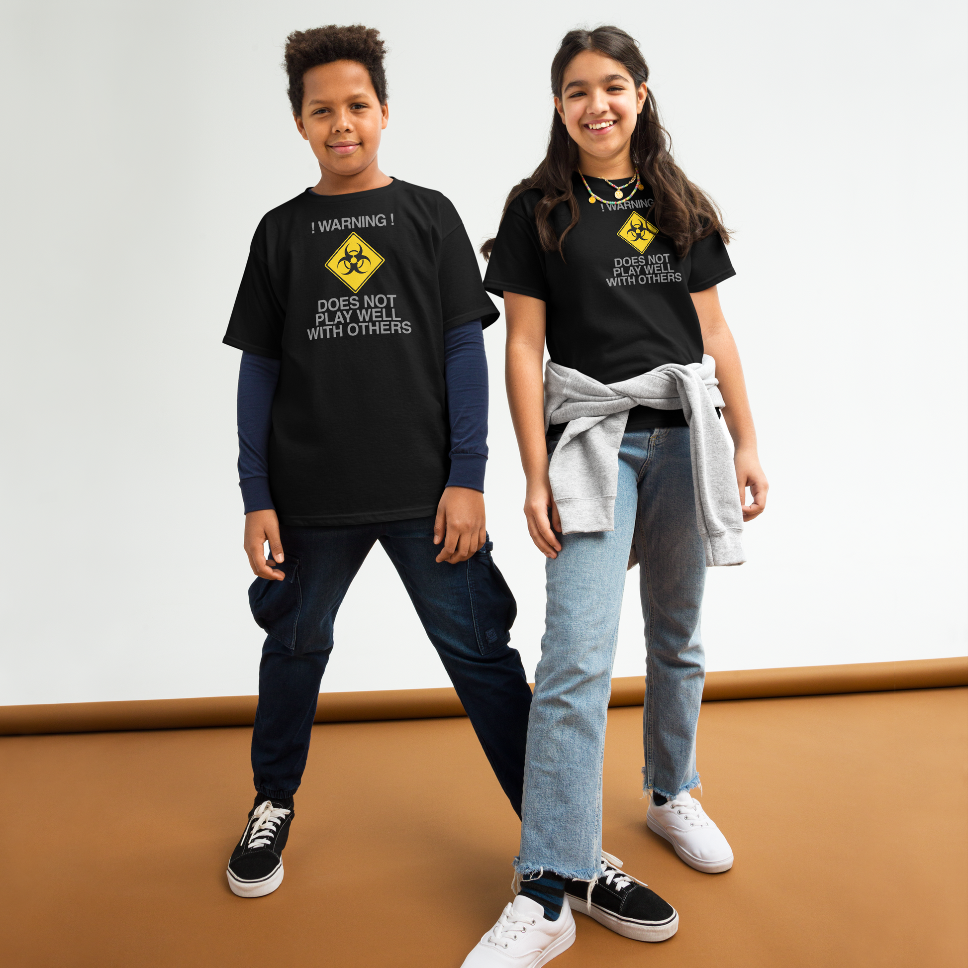 "!Warning! Does Not Play Well With Others" printed on a black youth classic tee worn by a female and male