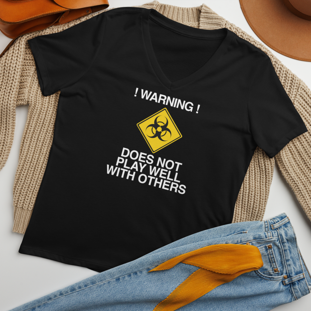 "!Warning! Does Not Play Well With Others" printed on a solid black blend women's relaxed v-neck t-shirt laying on a flat surface amongst other clothes