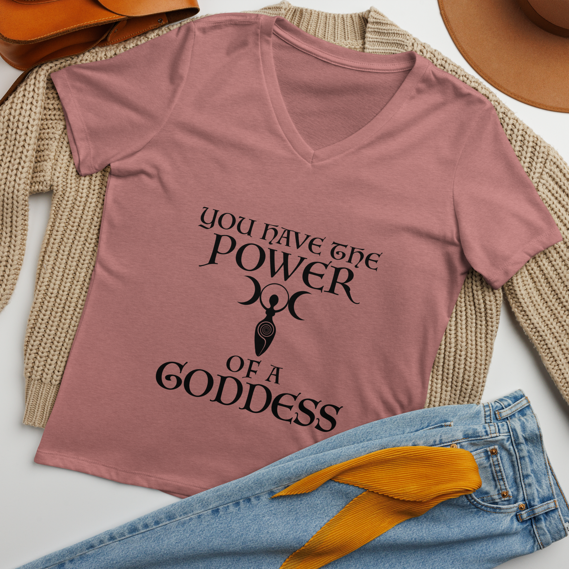 "You have the power of a goddess" printed on a heather mauve women's relaxed v-neck t-shirt laying on a flat surface amongst other clothes