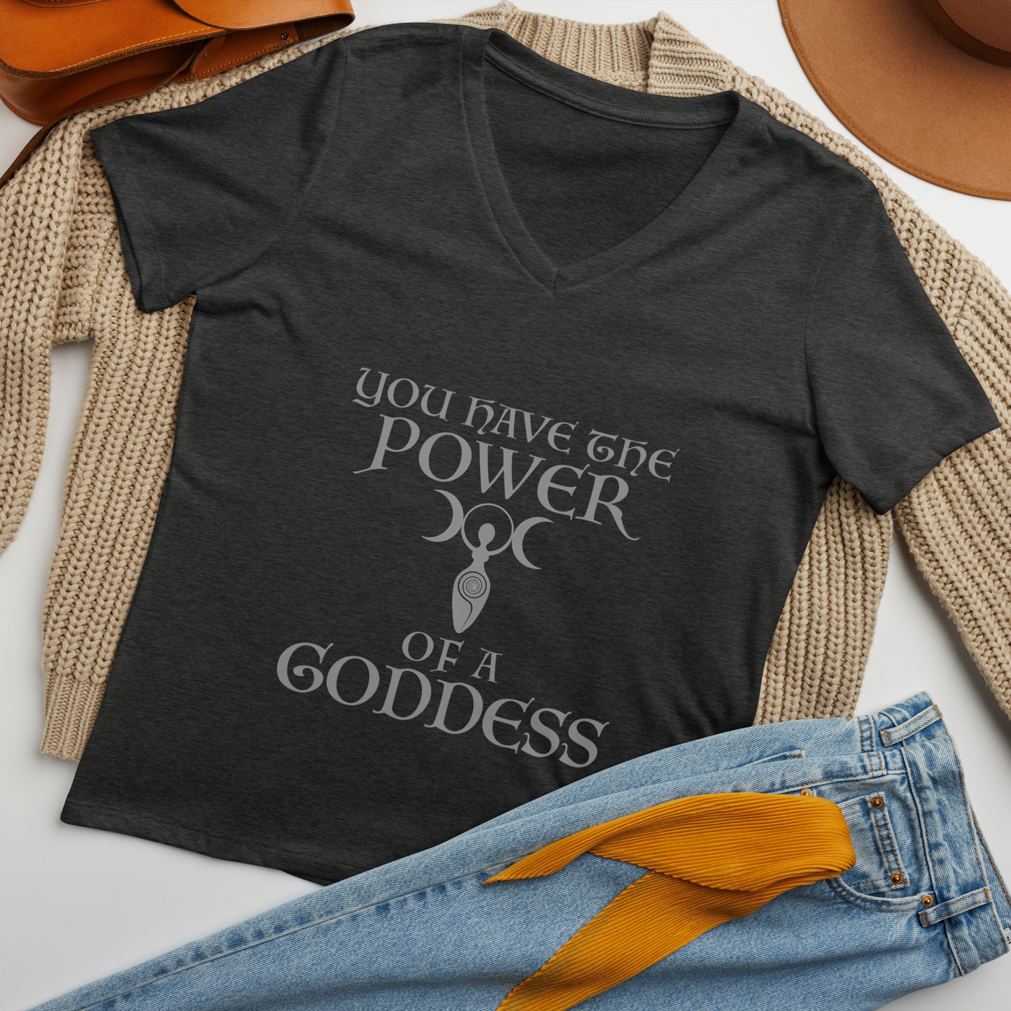 "You have the power of a goddess" printed on a dark grey heather women's relaxed v-neck t-shirt laying on a flat surface amongst other clothes