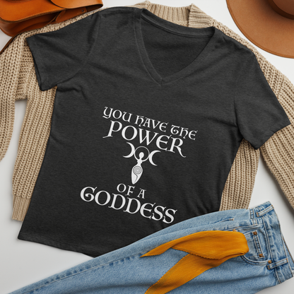 "You have the power of a goddess" printed on a dark grey heather women's relaxed v-neck t-shirt laying on a flat surface amongst other clothes