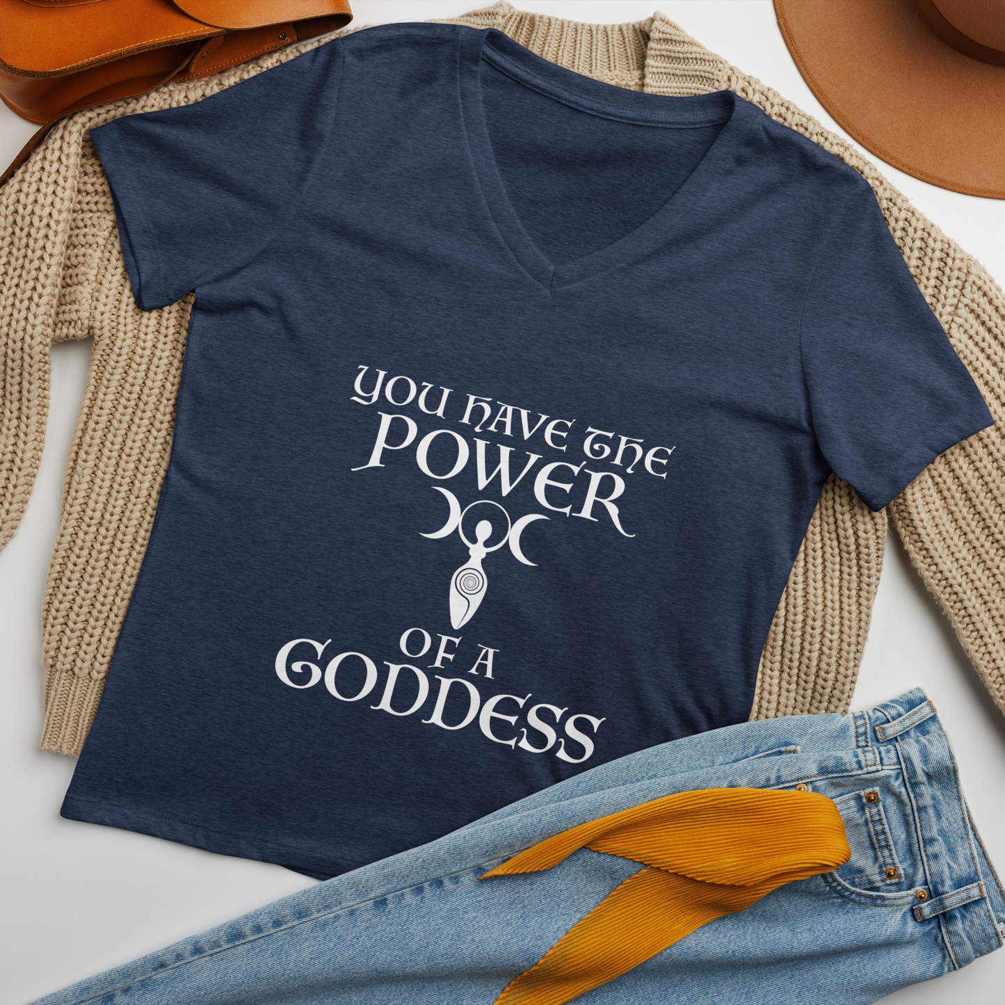 "You have the power of a goddess" printed on a heather navy women's relaxed v-neck t-shirt laying on a flat surface amongst other clothes