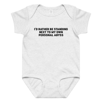 "I'd rather be standing next to my own personal abyss" printed on a ash baby jersey bodysuit laying on a flat surface amongst other clothes