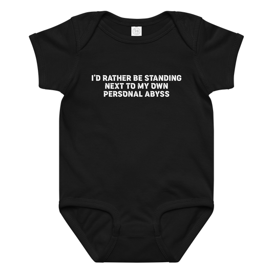 "I'd rather be standing next to my own personal abyss" printed on a black baby jersey bodysuit laying on a flat surface amongst other clothes