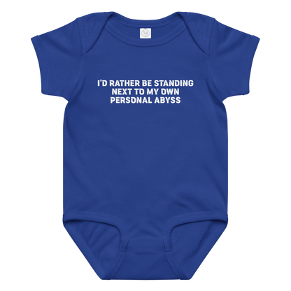"I'd rather be standing next to my own personal abyss" printed on a royal baby jersey bodysuit laying on a flat surface amongst other clothes
