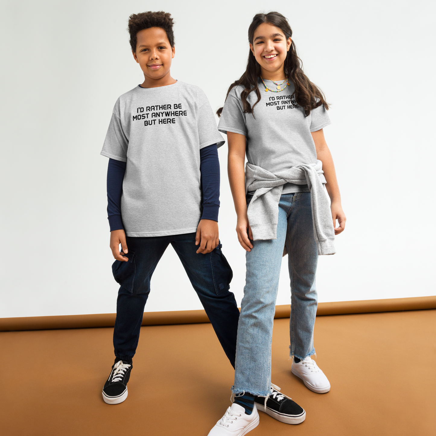"I’d rather be most anywhere but here" printed on a sport grey youth classic tee worn by a female and male