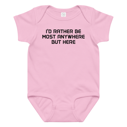 "I’d rather be most anywhere but here" printed on a pink baby jersey bodysuit laying on a flat surface amongst other clothes