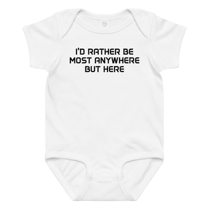 "I’d rather be most anywhere but here" printed on a white baby jersey bodysuit laying on a flat surface amongst other clothes