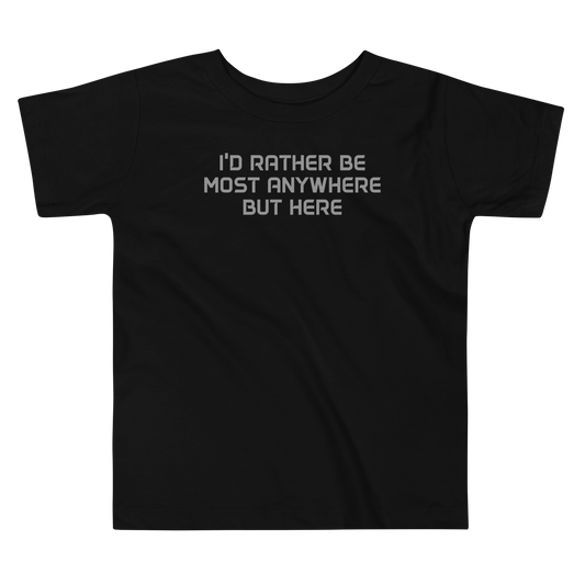 "I’d rather be most anywhere but here" printed on a black toddler short sleeve tee laying on a flat surface