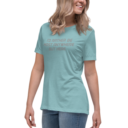 "I’d rather be most anywhere but here" printed on a heather blue lagoon women's relaxed t-shirt worn by a female
