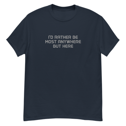 "I’d rather be most anywhere but here" printed on a navy unisex classic tee laying on a flat surface