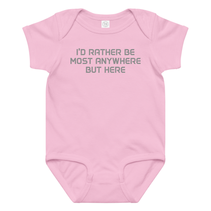 "I’d rather be most anywhere but here" printed on a pink baby jersey bodysuit laying on a flat surface amongst other clothes