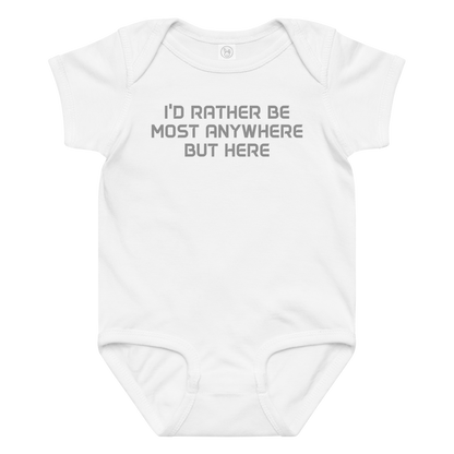 "I’d rather be most anywhere but here" printed on a white baby jersey bodysuit laying on a flat surface amongst other clothes