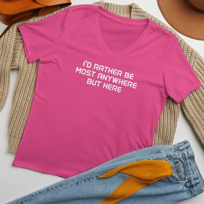 "I’d rather be most anywhere but here" printed on a berry women's relaxed v-neck t-shirt laying on a flat surface amongst other clothes