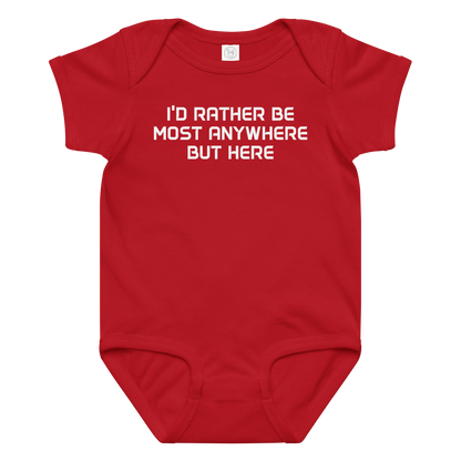"I’d rather be most anywhere but here" printed on a red baby jersey bodysuit laying on a flat surface amongst other clothes