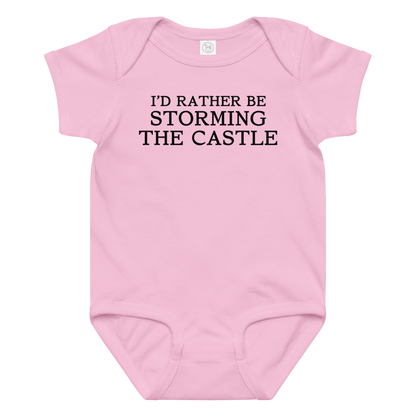"I'd rather be storming the castle" printed on a pink baby jersey bodysuit laying on a flat surface amongst other clothes