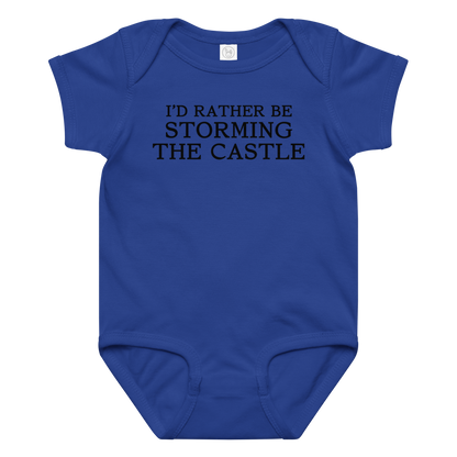 "I'd rather be storming the castle" printed on a royal baby jersey bodysuit laying on a flat surface amongst other clothes