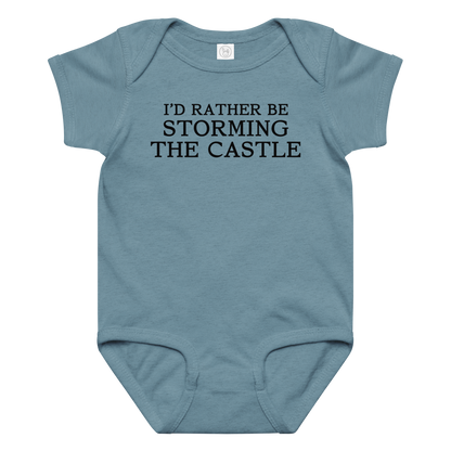 "I'd rather be storming the castle" printed on a vintage indigo baby jersey bodysuit laying on a flat surface amongst other clothes