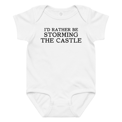 "I'd rather be storming the castle" printed on a white baby jersey bodysuit laying on a flat surface amongst other clothes