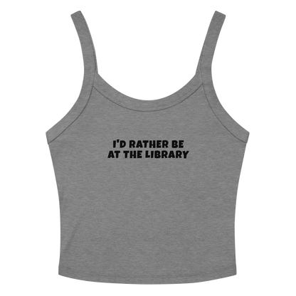 "I’d rather be at the library" printed on a athletic heather women's micro-rib tanktop laying on a flat surface amongst sunglasses and shorts