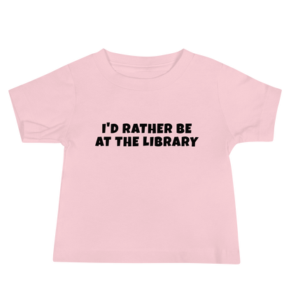 "I’d rather be at the library" printed on a pink baby jersey short sleeve tee laying on a flat surface