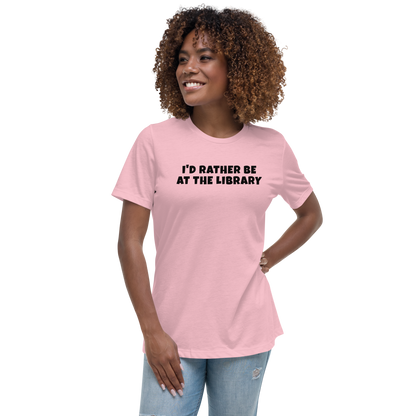 "I’d rather be at the library" printed on a pink women's relaxed t-shirt worn by a female
