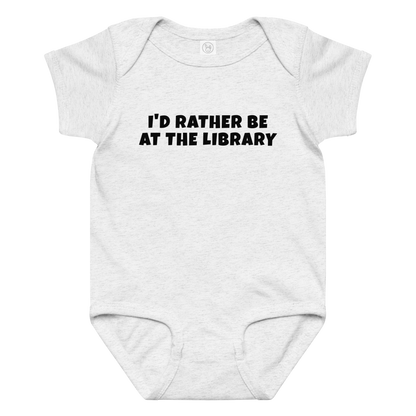 "I’d rather be at the library" printed on a ash baby jersey bodysuit laying on a flat surface amongst other clothes