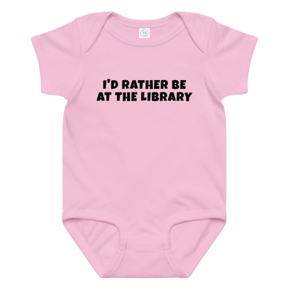 "I’d rather be at the library" printed on a pink baby jersey bodysuit laying on a flat surface amongst other clothes