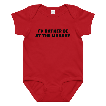 "I’d rather be at the library" printed on a red baby jersey bodysuit laying on a flat surface amongst other clothes