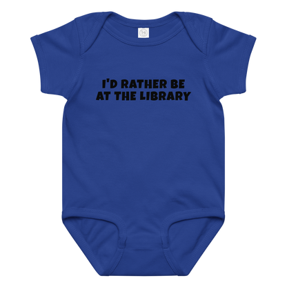"I’d rather be at the library" printed on a royal baby jersey bodysuit laying on a flat surface amongst other clothes